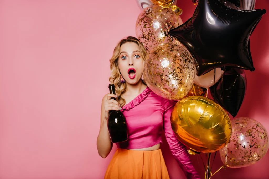 Woman holding a champagne bottle surrounded by party balloons