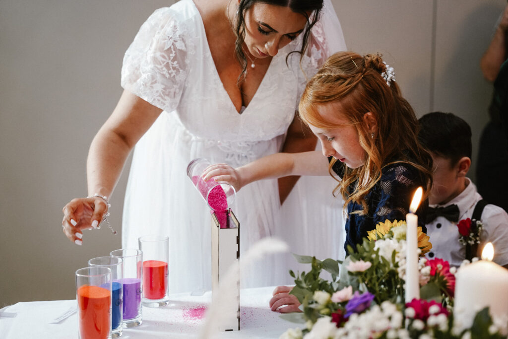 Bride and flower girl pouring coloured sand into a unity vase during a wedding ceremony