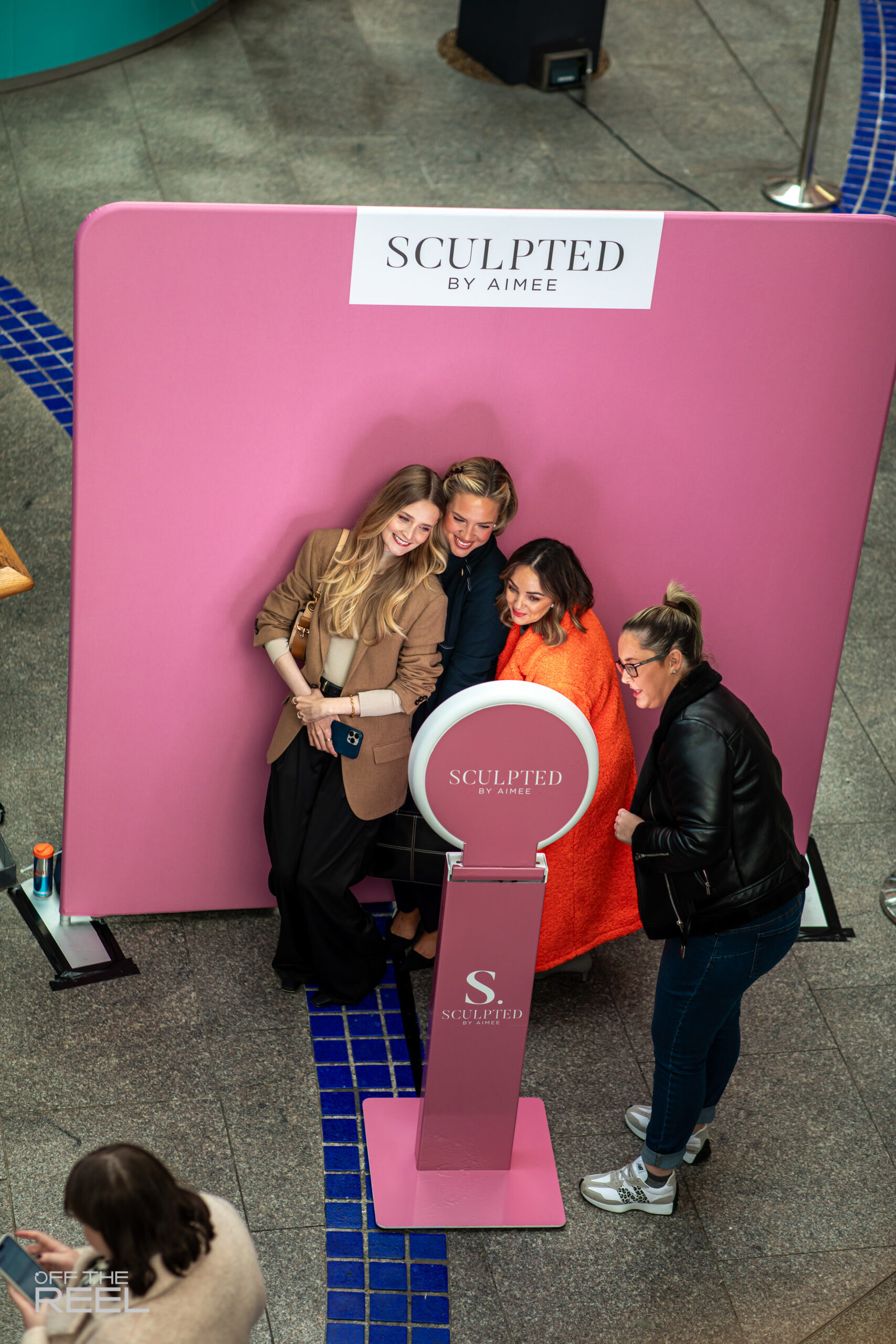 Group of guests posing at a branded pink photo booth backdrop