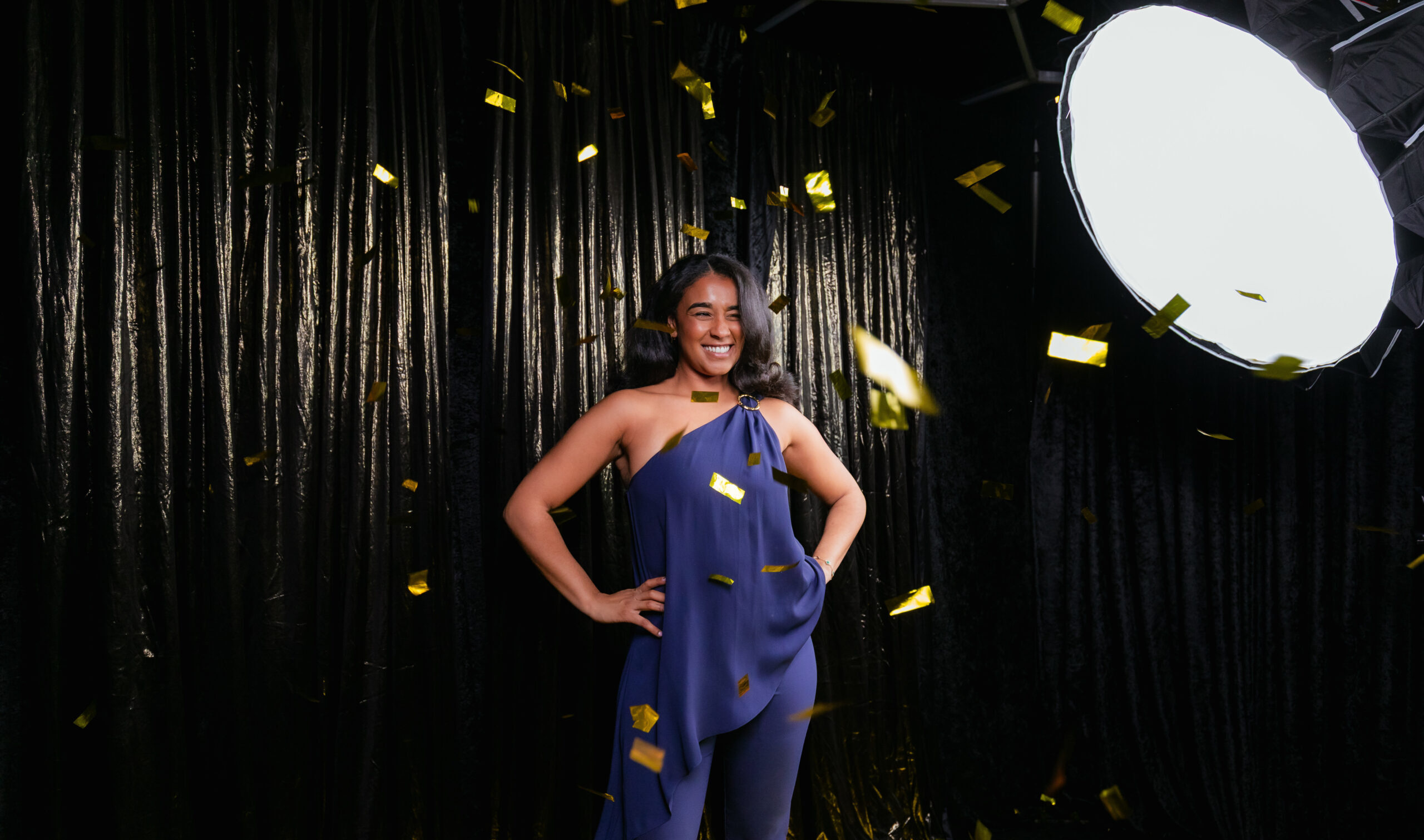 Woman posing under falling gold confetti in a photo booth setup